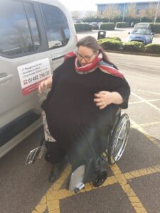 an overweight women sitting in a wheelchair next to a car.