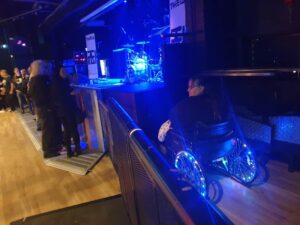 Helen in her chair with lighted wheels in a secure area next to the stage