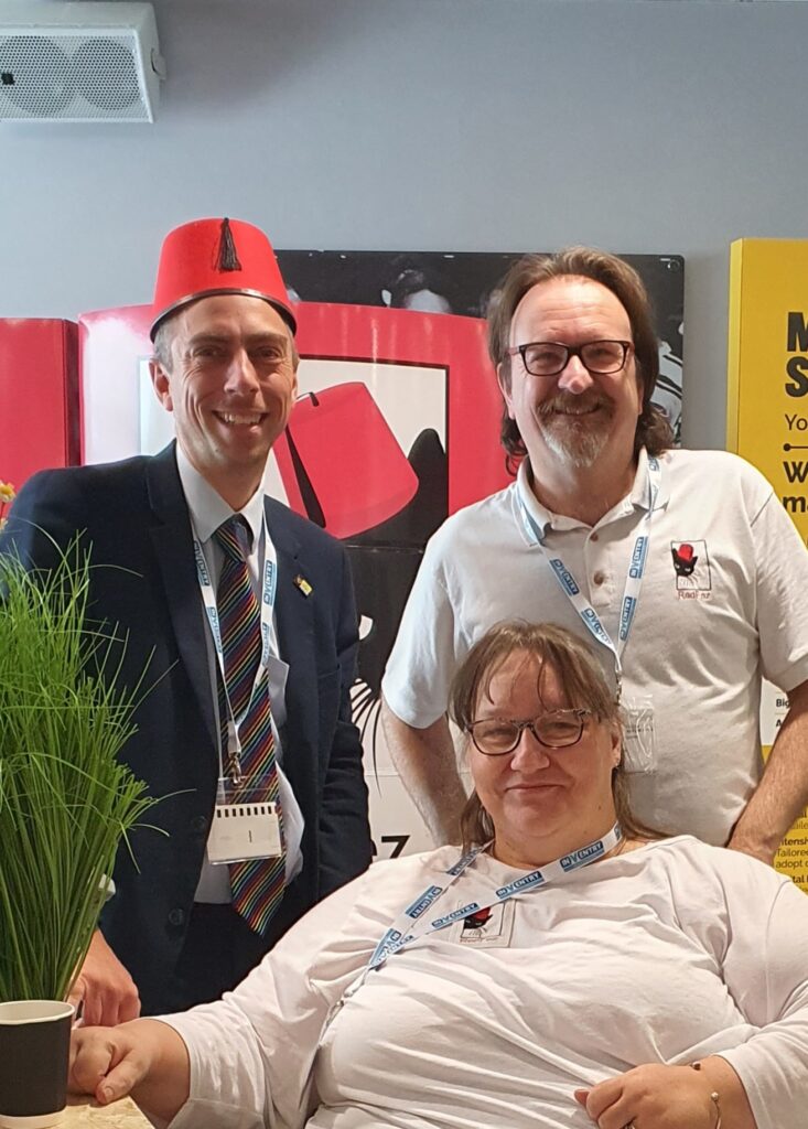 Three people posing for a photograph, one person wearing a fez