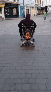 the back view of Helen on her powered chair as she rides on into the distance, Robin struggling to keep up